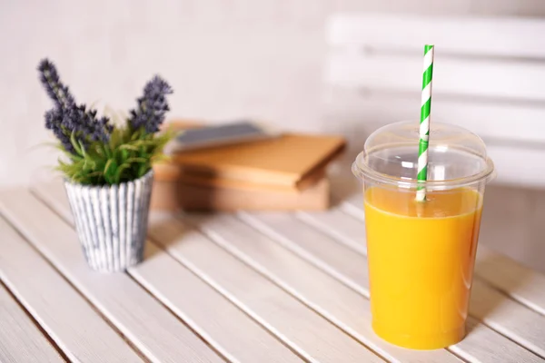 Orange juice in fast food closed cup with tube on wooden table with plant and light wall background — Stock Photo, Image