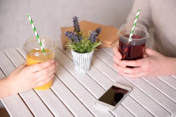 Twee vrouwelijke handen met fast-food kopjes SAP aan houten tafel met plant op de lichte muur achtergrond — Stockfoto