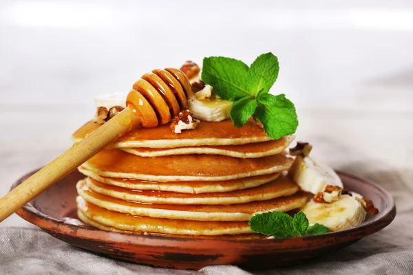 Pila di frittelle con menta, noci e fette di banana sul tavolo con tessuto su tavole di legno sfondo — Foto Stock