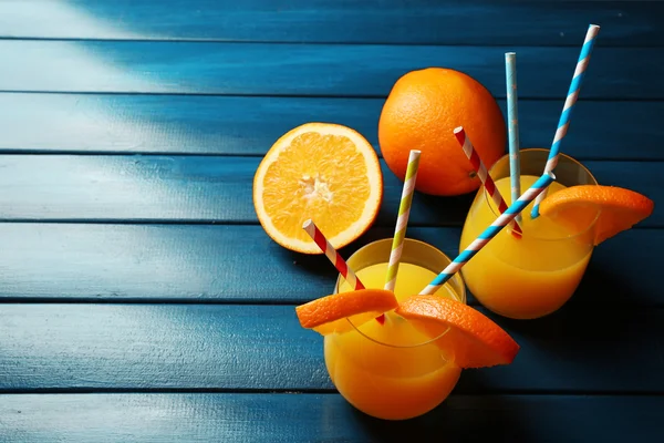 Vaso de zumo de naranja con pajitas y rodajas sobre fondo de madera de color —  Fotos de Stock