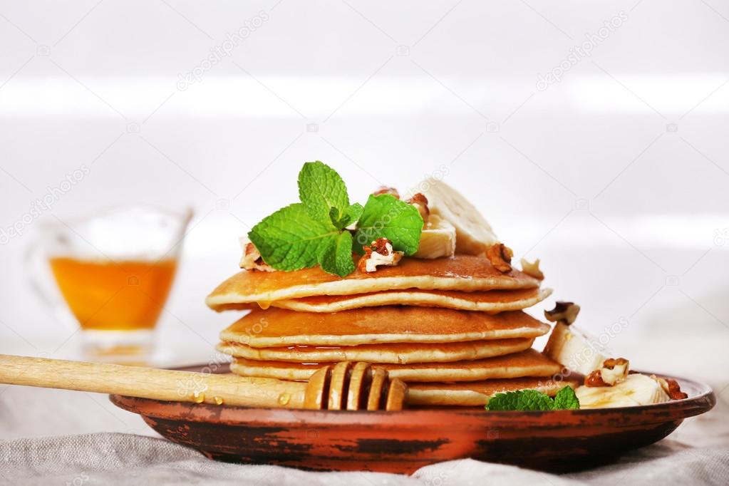 Stack of pancakes with mint, walnuts and slices of banana on table with fabric on wooden planks background