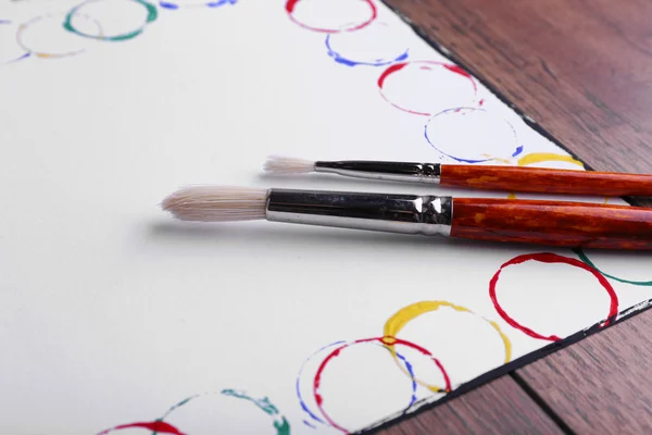 Färgglada penseldragen på pappersark och träbord bakgrund — Stockfoto