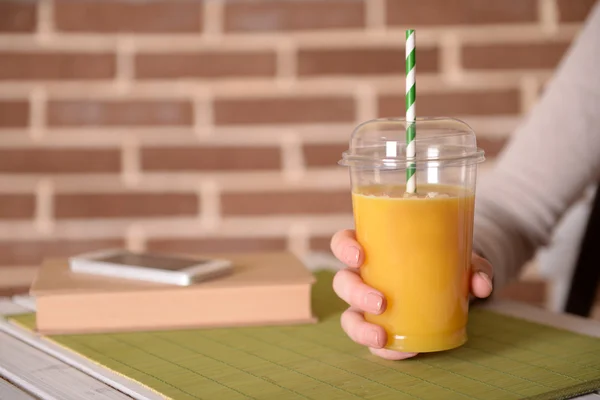 Female hand at table with fast food closed cup of orange juice on brick wall background