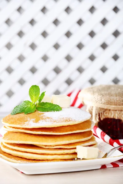 Pila di frittelle su piatto con banca di marmellata su tavolo e sfondo di reticolo di legno — Foto Stock