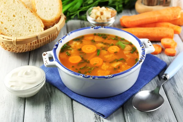 Composizione con zuppa di carote, ingredienti ed erbe su fondo di legno a colori — Foto Stock
