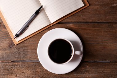 Fincan kahve üzerinde uçan daire ile defter ve kalem ahşap masa arka plan üzerinde