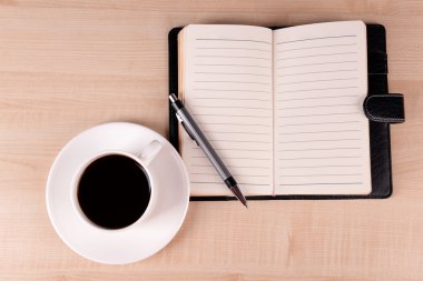 Fincan kahve tabağı ile günlüğü üzerinde ve ahşap masa arka plan üzerinde kalem