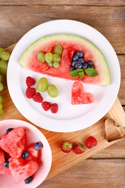 Fresh juicy watermelon slice  with cut out heart shape, filled fresh berries, on plate, on wooden background — Stock Photo, Image