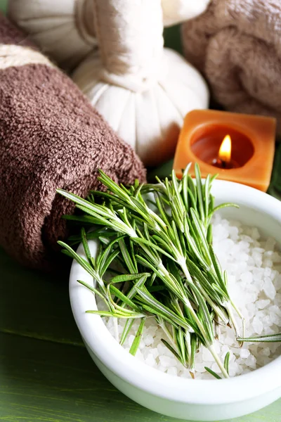 Branches of rosemary and sea salt in bowl, towels, candles and bottle with massage oil on wooden background. Rosemary spa concept — Stock Photo, Image