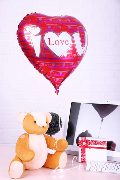 Teddybeer met huidige doos, plant en liefde hart ballon op houten computer tabel, op de bakstenen muur achtergrond — Stockfoto