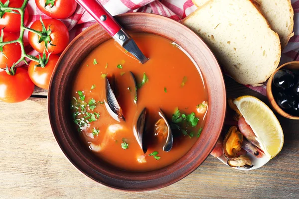 Leckere Suppe mit Garnelen, Miesmuscheln, Tomaten und schwarzen Oliven in einer Schüssel auf Holzgrund — Stockfoto