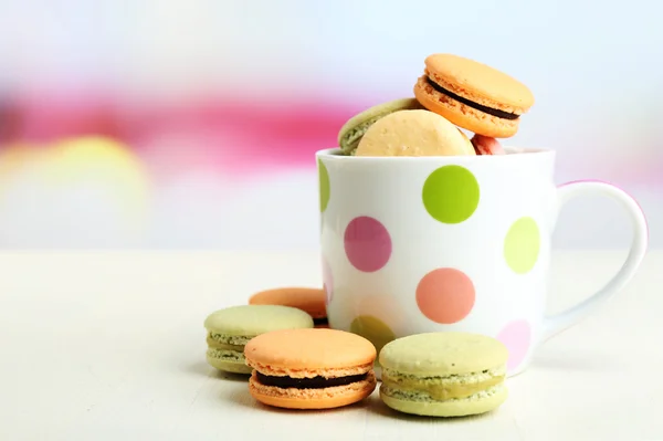 Assortment of gentle colorful macaroons in colorful mug on color wooden table, on light background — Stock Photo, Image