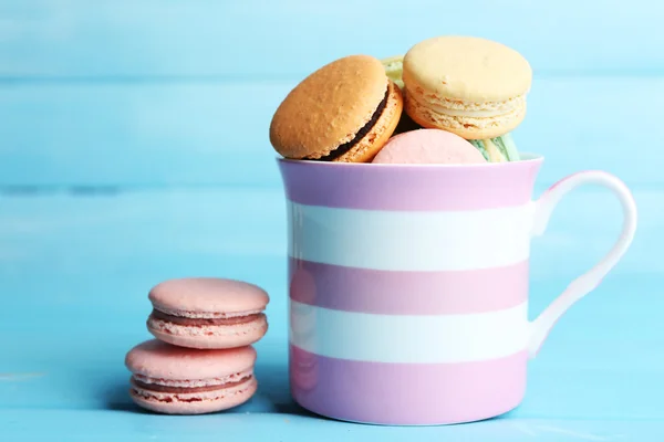 Sortiment av mjuka färgglada macaroons i färgglad mugg på färg trä bakgrund — Stockfoto