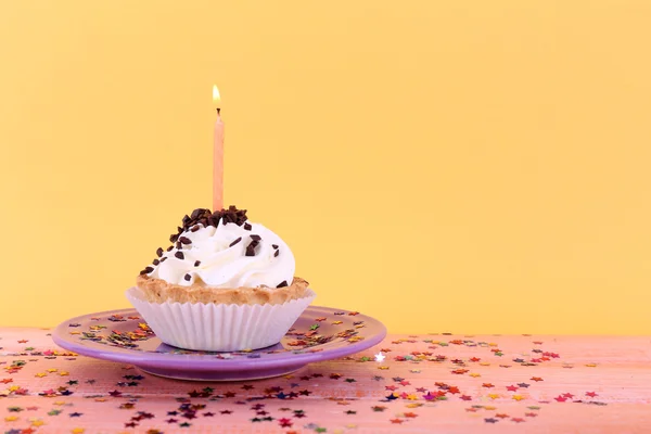 Cake van de kindverjaardag cup met kaarsen op plaat op kleur houten tafel en oranje achtergrond — Stockfoto
