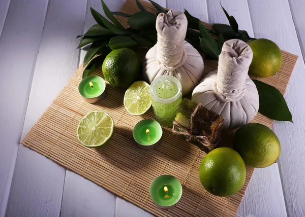Spa composition with lime and compress balls on bamboo mat and color wooden background — Stock Photo, Image