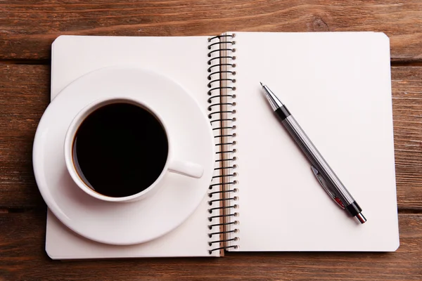 Xícara de café em pires com notebook e caneta sobre fundo de mesa de madeira — Fotografia de Stock