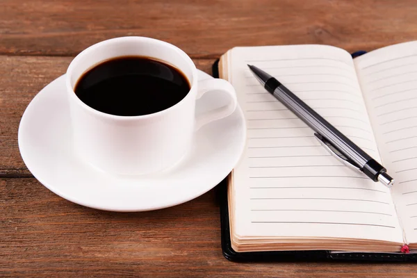 Taza de café en platillo con diario y pluma sobre fondo de mesa de madera — Foto de Stock