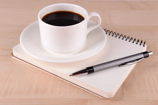 Taza de café en platillo con cuaderno y pluma sobre fondo de mesa de madera —  Fotos de Stock
