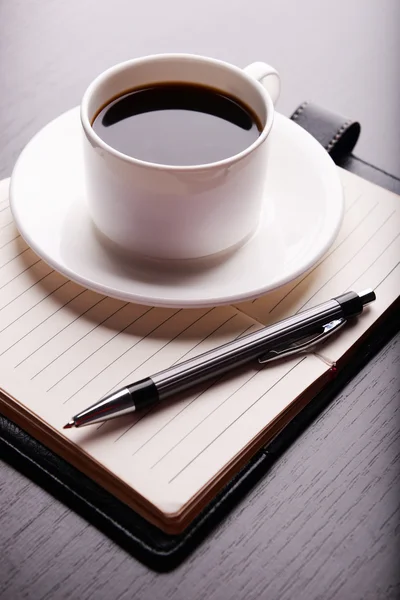 Taza de café en platillo con diario y pluma sobre fondo de mesa de madera — Foto de Stock