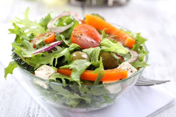 Griechischer Salat in Glasschale auf Serviette und farbigem Holzhintergrund — Stockfoto