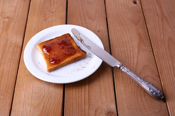 Ahşap masa arka plan üzerinde bıçak ile plaka üzerinde reçelli yaymak tost ekmeği — Stok fotoğraf