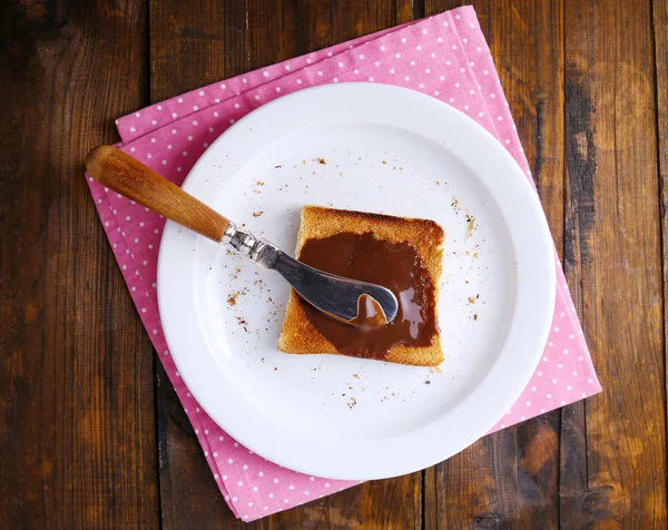 Toast brood uitgespreid met chocolade op plaat met mes en servet op houten tafel achtergrond — Stockfoto