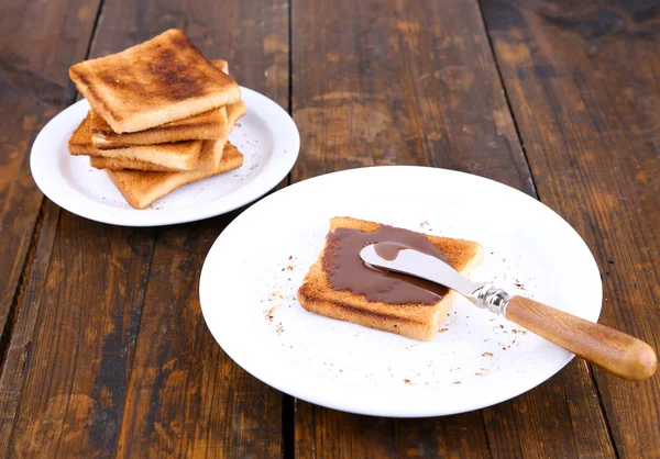 Pan tostado untado con chocolate en plato con cuchillo y servilleta sobre fondo de mesa de madera —  Fotos de Stock