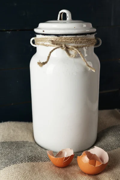 Milk can with eggshell on color wooden background — Stock Photo, Image