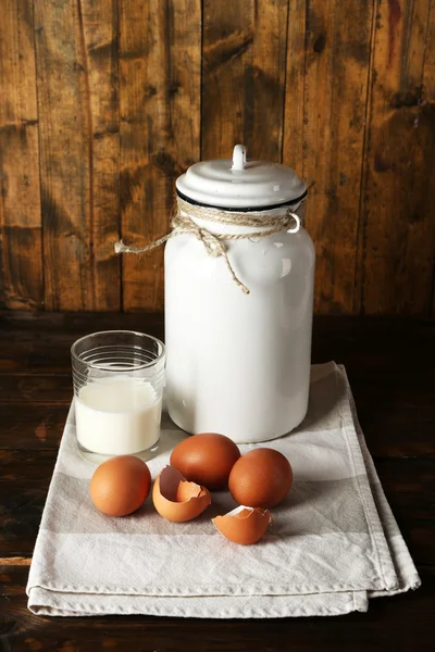 Milk can with eggs, eggshell and glass on rustic wooden background — Stock Photo, Image