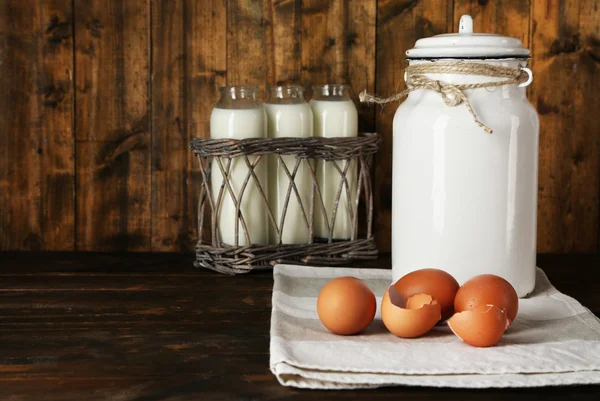 Boite de lait avec œufs, coquille d'oeuf et bouteilles en verre sur fond bois rustique — Photo