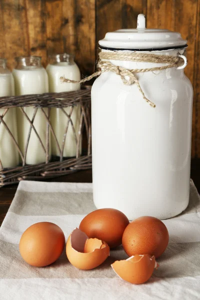 Milchkanne mit Eiern, Eierschalen und Glasflaschen auf rustikalem Holzgrund — Stockfoto