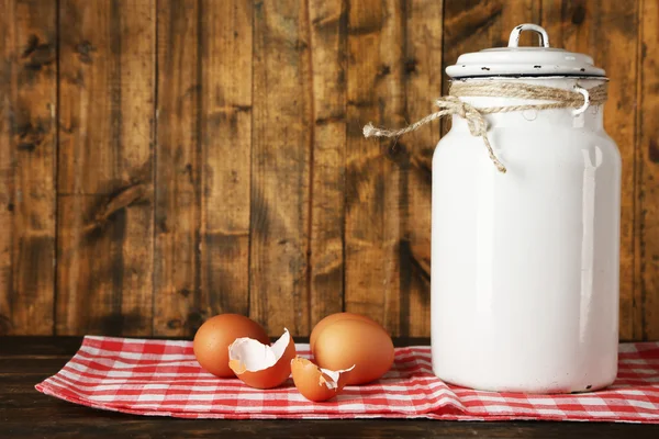 Latte lattina con uova e guscio d'uovo su tovagliolo su sfondo in legno rustico — Foto Stock