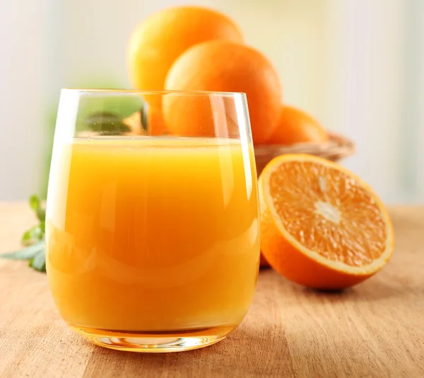 Glass of orange juice and wicker basket with oranges on wooden table background — Stock Photo, Image