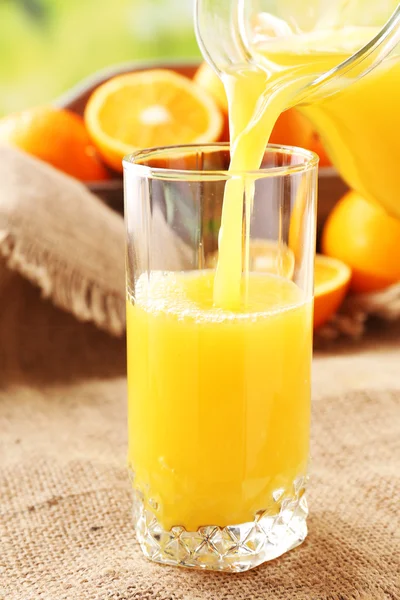 Pouring orange juice from glass carafe, on wooden table and bright background — Stock Photo, Image