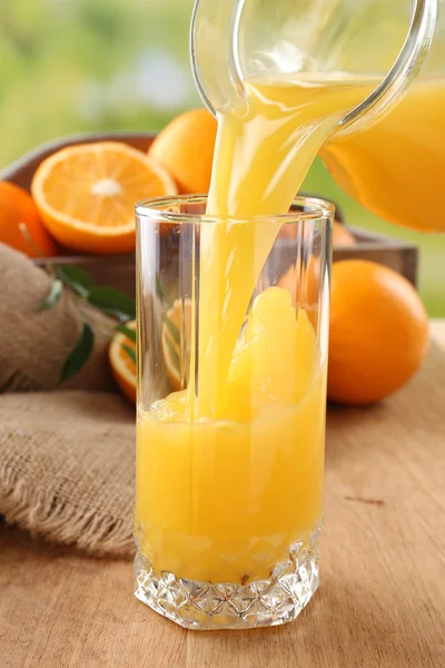Pouring orange juice from glass carafe, on wooden table and bright background — Stock Photo, Image