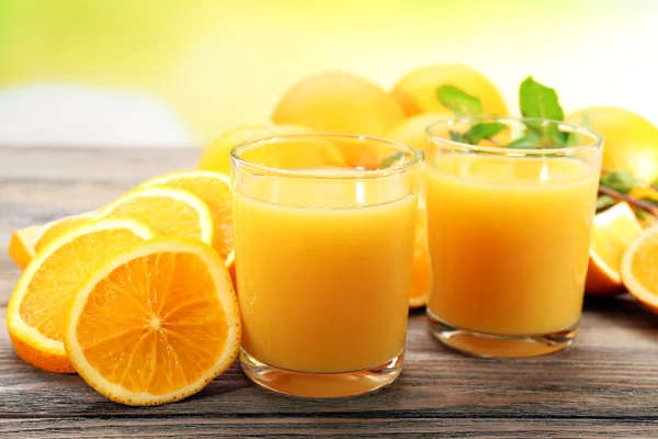 Vaso de zumo de naranja y rebanadas sobre mesa de madera y fondo brillante —  Fotos de Stock