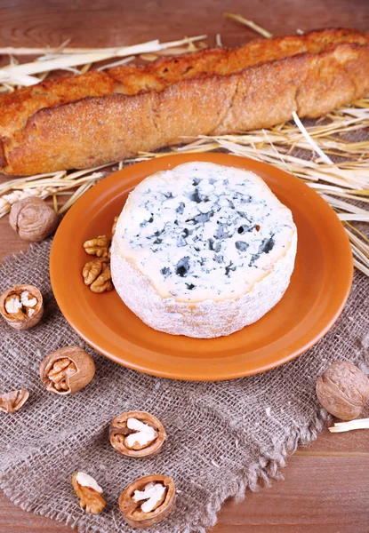 Синій сир на глиняній тарілці з горіхами, багет і сіно на тканині мішковини та дерев'яному фоні столу — стокове фото