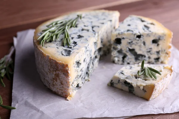 Blue cheese with sprigs of rosemary on sheets of paper and wooden table background — Stock Photo, Image