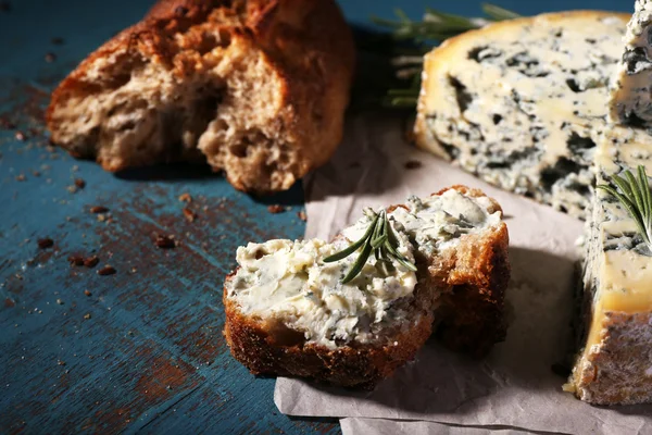 Fromage bleu avec brins de romarin et pain sur feuille de papier et fond de table en bois de couleur — Photo