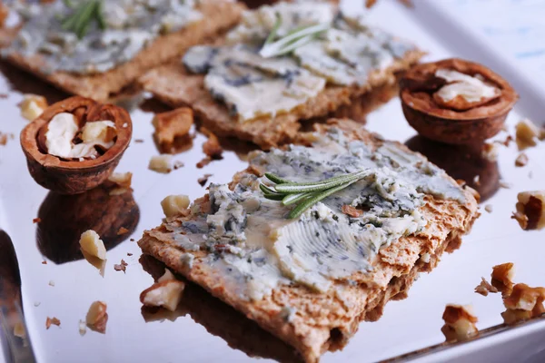 Crispbread with blue cheese, nuts and sprigs of rosemary on metal tray and color wooden table background — Stock Photo, Image