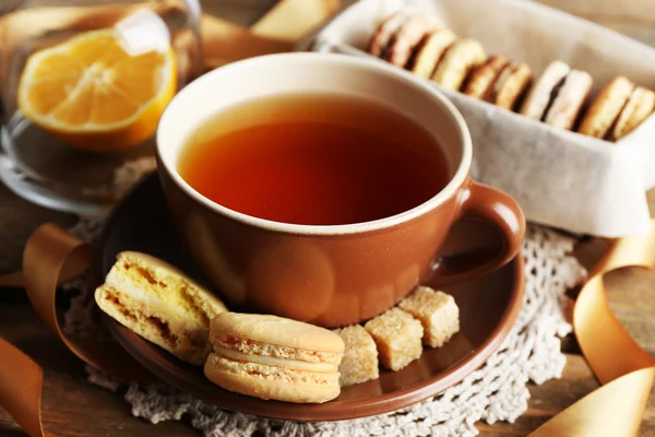 Bunte Makronen mit Tasse Tee auf hölzernem Hintergrund — Stockfoto