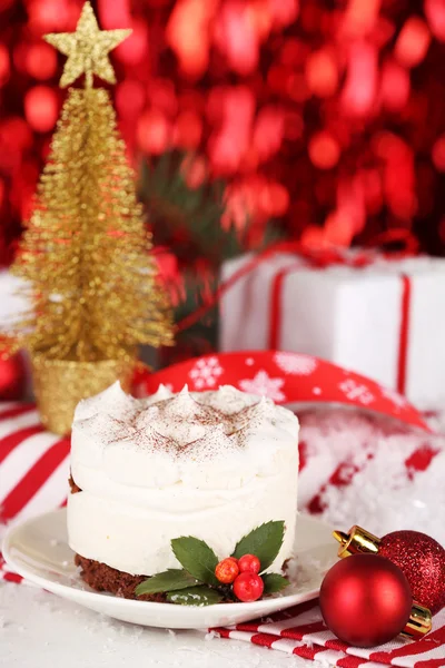Delicious cake on saucer with holly and berry on bright Christmas decoration background — Stock Photo, Image