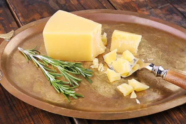 Crumbles Parmesan cheese with sprig of rosemary on metal tray on wooden table background — Stock Photo, Image