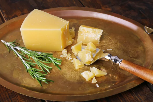 Crumbles Parmesan cheese with sprig of rosemary and blade on metal tray on wooden table background — Stock Photo, Image