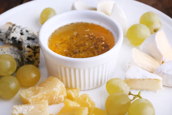 Diferentes tipos de queijo com uva e pires no prato em fundo de mesa de madeira — Fotografia de Stock
