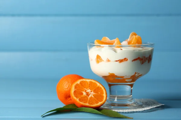 Dessert au lait savoureux avec des morceaux de mandarine fraîche dans un bol en verre, sur fond de bois de couleur — Photo