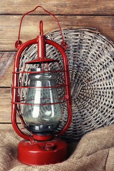 Kerosene lamp with wicker mat and burlap cloth on wooden planks background — Stock Photo, Image