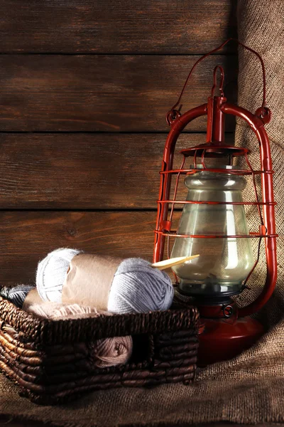 Lámpara de queroseno con hilo y agujas para tejer en canasta de mimbre sobre fondo de madera — Foto de Stock