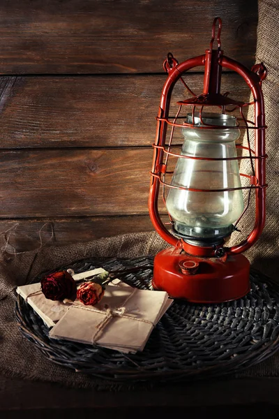 Kerosene lamp with dried rose and letter on wicker mat and wooden planks background — Stock Photo, Image