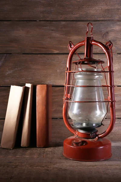 Lámpara de queroseno con libros sobre fondo rústico de madera — Foto de Stock